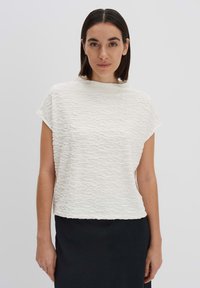 Top bianco testurizzato con collo alto e maniche corte, caratterizzato da un motivo ondulato e una vestibilità comoda, abbinato a una gonna scura.