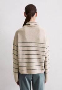 Beżowy sweter z pionowymi zielonymi pasami, z wysokim kołnierzem i luźnym krojem. Miękka tekstura, ściągacze przy mankietach i wykończeniu.