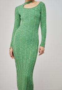 Abito verde a maniche lunghe con righe, caratterizzato da un dettaglio con spalle scoperte, con una silhouette aderente e un tessuto strutturato.