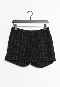 Svarta shorts med rutmönster, gjorda av texturerad tyg, med framfickor och en lätt uppvikt fåll, hängande på en svart galge.