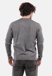 Maglione grigio a maglia con motivo a trecce sulle spalle, scollo rotondo e polsini a coste. Indossato sopra jeans neri, visto da dietro.