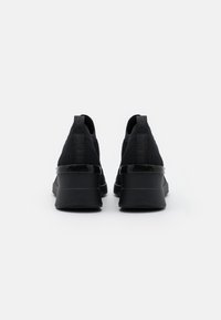 Black sneakers with a textured knit upper and a glossy, chunky sole. Features pull tabs at the heel and minimalistic design elements.