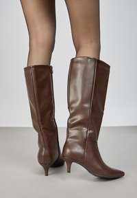 Bottes marron en cuir jusqu'au genou avec un bout pointu et un talon fin. Elles présentent une surface lisse et une fermeture éclair latérale pour une mise en chaussure facile.