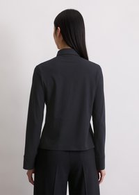 Maglietta nera a maniche lunghe con colletto, realizzata in tessuto liscio, forma aderente e leggera curvatura all'orlo. Presenta dettagli minimi.