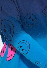 Camicia a maniche lunghe con gradiente blu, caratterizzata da motivi di facce sorridenti nere e accentuata da sorrisi rosa sul davanti, realizzata in cotone.