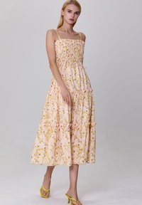 Robe maxi à imprimé floral en rose avec un corsage smocké, de fines bretelles et un ourlet volanté. Présente des motifs de fleurs jaunes tout au long.