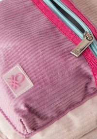 Fialové texturované pouzdro s růžovým zipem, modrým akcentem a průhlednou štítkem s růžovým symbolem. Měkká látka s žebrovaným vzorem.