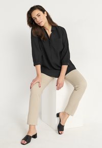 Svart, strukturerad blus med krage, knappdetalj och bröstficka. Tillsammans med beige slim-fit byxor och svarta klackiga mule-skor.