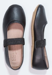 Svarte Mary Jane-sko med glitrende elastiske stropper og beige polstrede såler, vist fra top- og sidevisning på hvit bakgrunn.