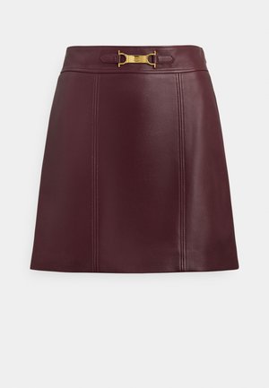 Burgundska usnjena krilo z ravnim krojem, ki ima zlato zaponko v pasu in subtilne šive za teksturo.