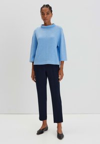 Pullover azzurro chiaro con collo a imbuto, caratterizzato da una vestibilità rilassata e maniche a tre quarti, abbinato a pantaloni navy aderenti e scarpe nere.