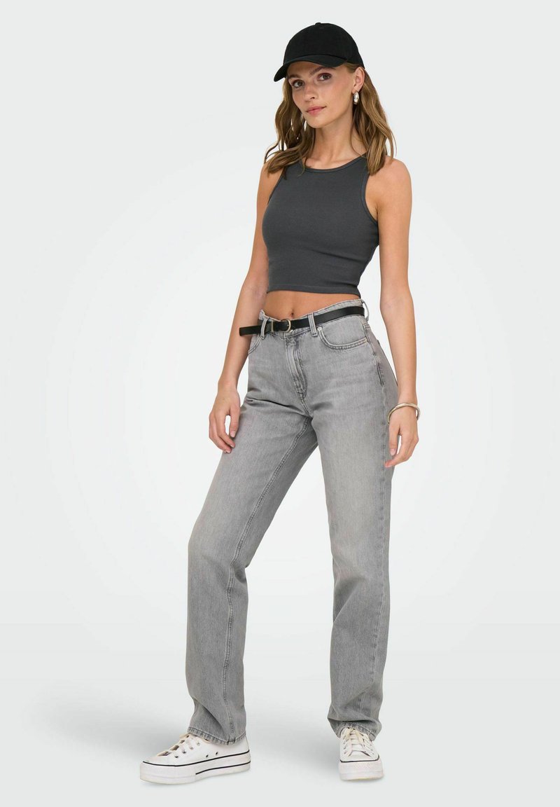 Grå cropped tank top, lysegrå straight-leg jeans, sort bælte og hvide sneakers. Modellen har en sort kasket og sølvøreringe på.