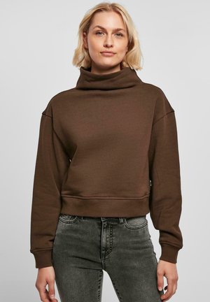 Brun cropped sweatshirt med høy krage, laget av myk stoff, med senkede skuldre og ribbestrikkede mansjetter. Kombinert med mørke jeans.