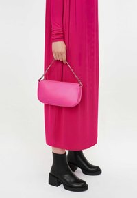 Roosa nahast käekott kettkäepidemega, sile tekstuur, ristkülikukujuline; sobitatud pika roosa kleidi ja mustade pahkluu saapadega.