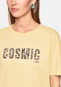 Yellow cotton t-shirt featuring "COSMIC" in zebra-striped letters and "LOVE" in rhinestones. Simple crew neckline and short sleeves.