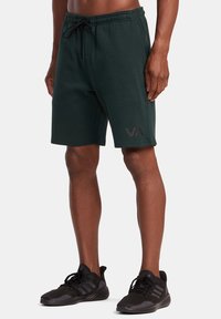 Shorts en polaire vert foncé avec une taille élastique, un cordon de serrage, des poches latérales et un grand logo gris accentuant la jambe inférieure.