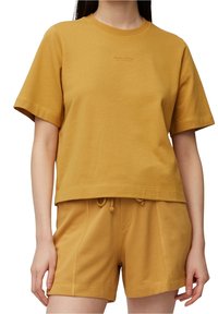 Camiseta de algodón color mostaza con mangas cortas, cuello redondo y dobladillo recto. Se lleva con pantalones cortos a juego en color mostaza con cintura elástica.