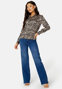 Camicia a maniche lunghe con bottoni di colore beige con strisce zebrate nere, abbinata a jeans a vita alta blu svasati. Tessuto morbido, vestibilità casual.