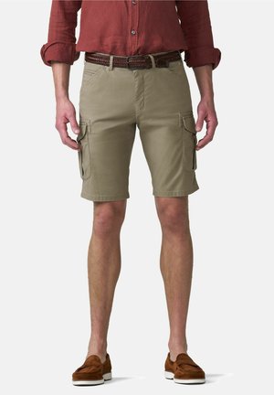 Man draagt beige cargoshorts, een bruine gevlochten riem, een roestkleurig opgerolde overhemd en bruine instapschoenen tegen een witte achtergrond.
