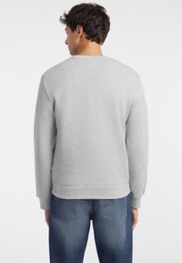 Sudadera gris de cuello redondo con puños y dobladillo acanalados. Textura suave con un corte relajado, combinada con jeans de mezclilla azul.
