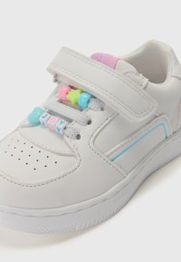 Baskets blanches pour enfants avec une sangle en velcro, perles pastel sur les lacets écrivant "JOY" et languette rembourrée rose avec un détail bleu sur le côté.