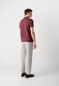 Bordová polokošeľa s krátkymi rukávmi, v kombinácii s svetlošedými nohavicami a čiernymi topánkami, z pohľadu zozadu. Jednoduchý a čistý dizajn.