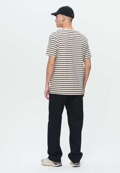 Beżowo-czarny t-shirt w paski, krótki rękaw, luźny krój, zestawiony z czarnymi spodniami i szarymi trampkami, widok z tyłu.