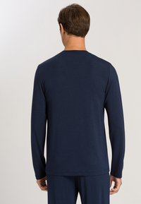 T-shirt a maniche lunghe in tessuto blu navy scuro con una superficie liscia. Presenta un collo a giro e una vestibilità rilassata. Nessun motivo o accento visibile.