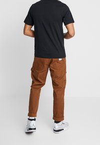 Camiseta negra de algodón combinada con pantalones cargo marrones, con puños enrollados y bolsillos laterales, complementados con zapatillas de baloncesto blancas y grises.