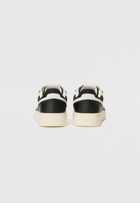 Paire de baskets basses noires et blanches vues de dos sur un fond clair uni.