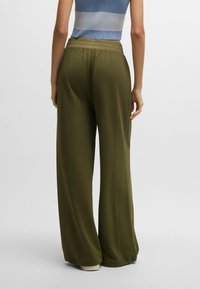 Grüne weite Hosen aus einem glatten, leichten Stoff mit elastischem Bund, die einen lockeren Sitz und minimale Nähte aufweisen.