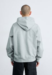 Sweat-shirt à capuche grise avec une coupe décontractée. Présente une poche kangourou avant et des poignets côtelés, affiché de dos.