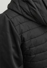 Close-up of a black quilted jacket back with a padded hood and smooth black fabric sleeves.