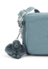 Light blue fabric shoulder bag with a silver clasp and textured surface, featuring a gray plush gorilla keychain attached.