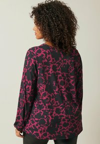 Langmouwtop met een zwarte basis en grote abstracte roze bloempatronen, gemaakt van zachte stof met een relaxte pasvorm en ronde halslijn.