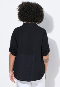 Schwarze, leichte Bluse mit einem Kragen, hochrollbaren Ärmeln und einem leicht durchsichtigen Rücken, mit einem lockeren Schnitt und abgerundetem Saum.
