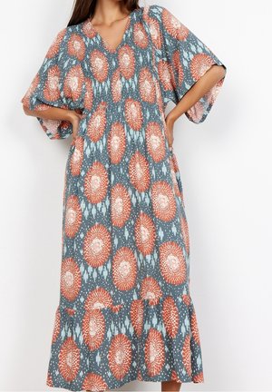 Blauwe jurk met oversized mouwen, V-hals en een bloemenpatroon van oranje en witte cirkels op een gestructureerde achtergrond.