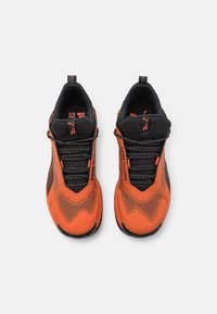Des chaussures de sport avec une tige en maille noire et orange, des superpositions synthétiques texturées, des lacets élastiques et un col rembourré pour plus de confort.
