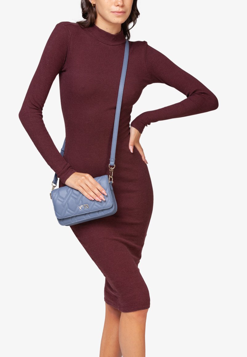 Bordeaux geribde jurk met lange mouwen en een getailleerde silhouette. Blauw gewatteerde schoudertas met verstelbare band en metalen accenten.