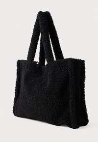Zwarte totebag met een pluche, textuurrijke buitenkant, twee stevige handvatten en een rechthoekige vorm. Zacht materiaal met een dichte, fuzzy stof.