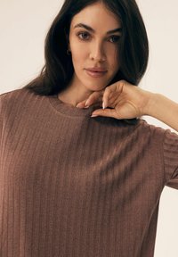 Brązowy, prążkowany top z dzianiny z okrągłym dekoltem, z krótkimi rękawami i luźnym krojem. Miękka tekstura i subtelny połysk widoczne.
