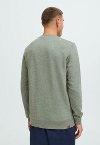 Herresweater i heathered olivengrønn. Har rund hals, lange ermer, strukturert stoff og et lite logo-patch nær kanten.