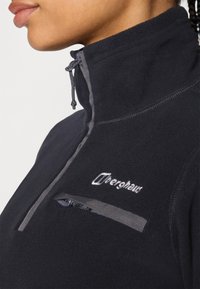 Pullover in pile nero con colletto alto, dettaglio zip grigio e una piccola tasca sul petto con zip. Presenta un logo ricamato sul fronte.