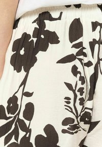Tessuto a fantasia floreale con grandi fiori marrone scuro su uno sfondo crema. Materiale leggero e con texture, dotato di una vita elastica.