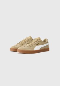 Beige ruskind sneakers med hvid sideaccent og guld logo. Flad brun gummisole. Snøresystem med polstret krave og lav profil.