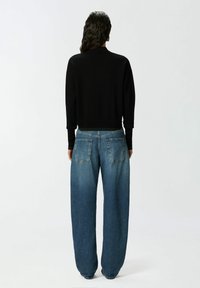 Crna dugotrajna majica u paru sa širokim plavim trapericama. Traperice imaju dva stražnja džepa i izblijedjeli izgled. Ukupni dizajn je jednostavan.