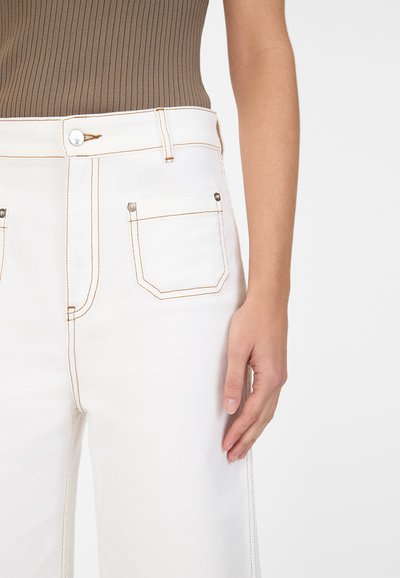 Hvite denim bukser med oransje syninger, med knapp foran, to sidelommer og en baklomme i rektangulær form.