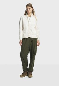 Veste zippée en polaire crème, associée à un pantalon cargo olive ample et des bottes brunes à lacets. Dotée de coutures plates et de poches latérales.