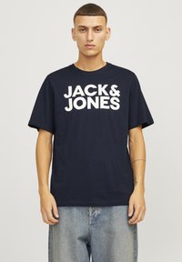 Tricou de culoare bleumarin, cu text alb "JACK & JONES" scris cu litere îngroșate. Mânici scurte, decolteu rotund, fabricat din material de bumbac. Croială casual.