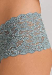 Mutandine di pizzo con una fascia blu-verde ondulata decorata con motivi floreali, realizzate in delicato pizzo con una texture trasparente.